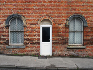 white front door and windows of a typical old brick british terraced house with arched windows and net curtains