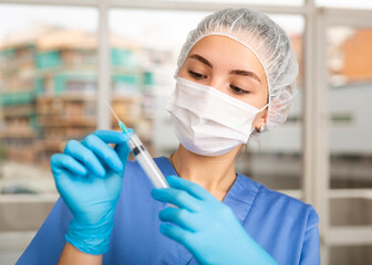 Portrait of nurse in medical cap and protective face mask with syringe in her hands