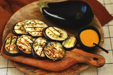 Grilled eggplant on a wooden board with honey mustard sauce.