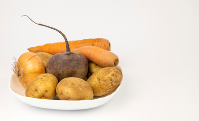 Vegetables: yellow onions, potatoes, beets, carrots laid out on a white plate, on a white background, a set of products for cooking borscht.