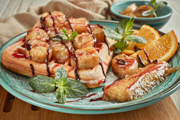 Tasty waffles with caramelized banana, mint, jam and sweet sauce on plate on wooden background.  Sweet meal. Dessert