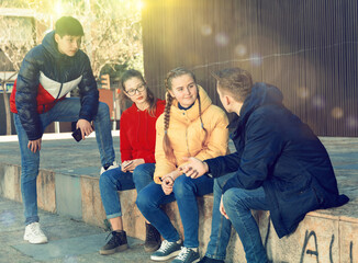 Four teenagers enthusiastically look at the screens of their smartphones on city street