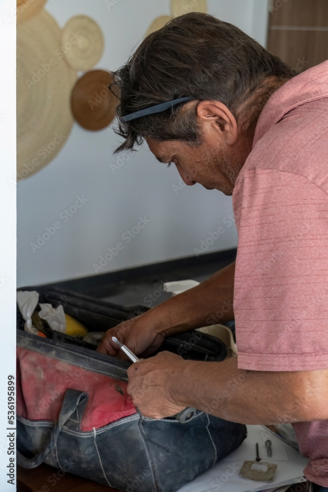 Wall mural latino man looking for tools in his toolbox, hispanic, with screwdriver in hand