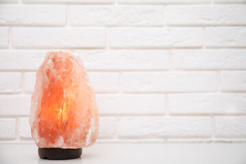 Himalayan salt lamp on table near white brick wall. Space for text