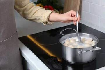 Woman cooking dumplings in saucepan with boiling water on cooktop, closeup