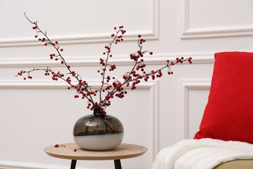 Hawthorn branches with red berries in vase on table near white wall indoors