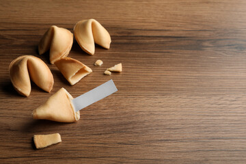 Tasty fortune cookies and paper with prediction on wooden table, space for text
