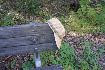 Woven Straw Cap with Visor Hanging from Corner of Weathered Wood Bench