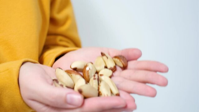 Girl in a yellow sweatshirt holds brazil nut in her hands close-up on a white background.