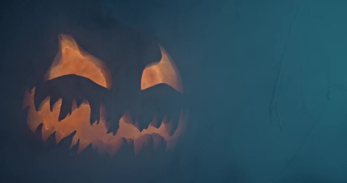 Spooky Halloween jack o lantern with glowing scary face carved out of a pumpkin and surrounded by smoke and mist.