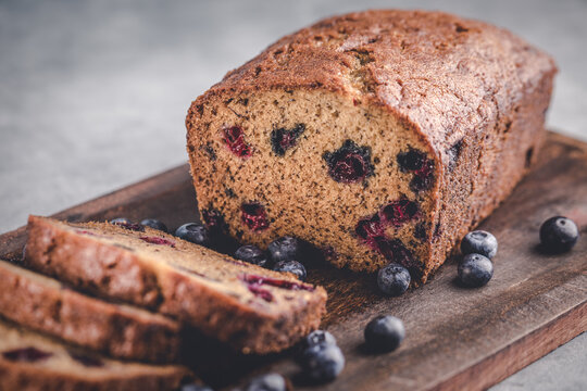 Loaf of homemade sliced blueberry banana bread with blueberries on a wooden cutting board