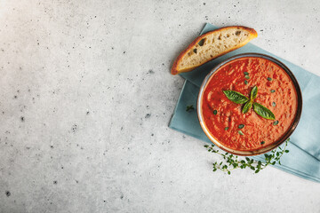Top view of a bowl of fresh homemade tomato basil soup with fresh herbs and slice of focaccia bread with space for text