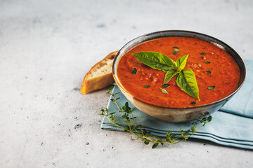 Bowl of fresh homemade tomato basil soup with fresh herbs and slice of focaccia bread with space...