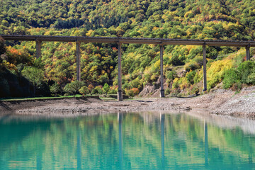 Scenic view on the lake with blue water and bridge on background of mountains in autumn season. Caucasus Mountains, Georgia.