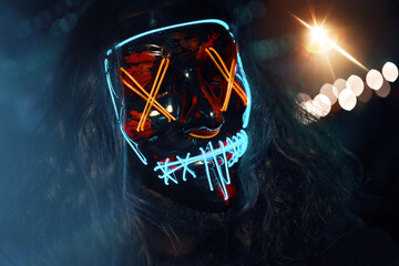 Man with long disheveled hair in a lighting neon glowing mask. Halloween dress-up party. Anonymous...