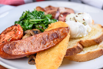 A serving of country breakfast consisting of bacon, tomato, eggs, toast, mushrooms, spinach, spinach and a hash brown