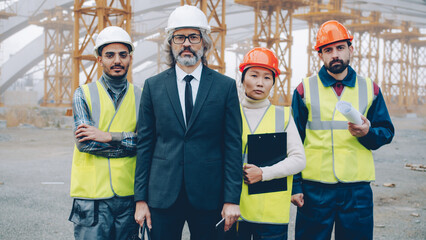Multi-ethnic group of people builders standing outdoors in industrial site and looking at camera....
