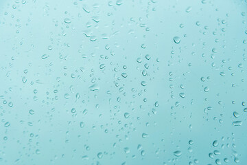 Raindrops on window glass against blue autumn sky. Abstract texture.