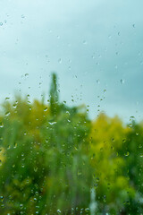 Raindrops on window glass against  background of colorful autumn trees in park. Abstract texture.