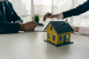 A real estate agent or broker meets with clients, discusses a property purchase and insurance contract, with examples of homes on the side and on hand.