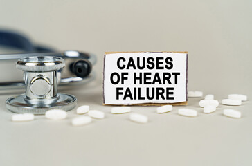 On a gray background, a stethoscope, pills and a cardboard plate with the inscription - Causes of heart failure