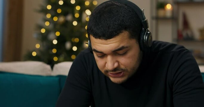 Upset man listening to music in headphones. He is wearing black sweater. Song he was listening to with his ex is playing in headphones. Man sings along in frustration, because he misses the girl.