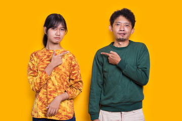 young asian couple pointing with fingers to each other isolated on yellow background
