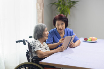 Elderly woman reading aloud a book for dementia therapy with caregiver. - 536231491