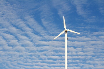 wind turbine for generating electricity on sky background and white clouds