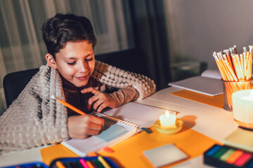 Little boy studying in low light with a burning candle.  Power outage, energy crisis concept.