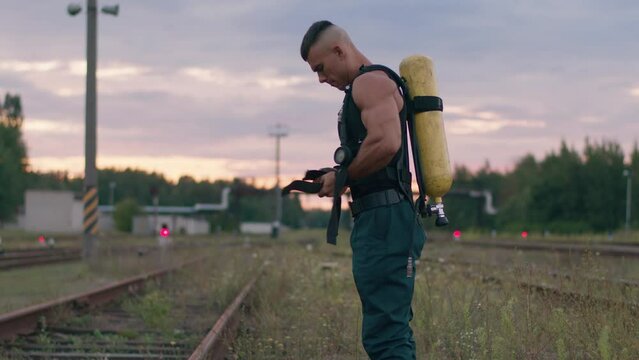 Young muscular man in black sleeveless t-shirt stands on the railroad tracks and puts balloon drager on his back. Slow motion