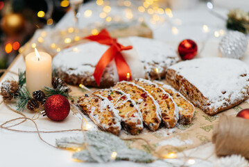 Traditional German Christmas stollen made of dried fruits and nuts, sprinkled with powdered sugar on the background of a Christmas decor with candles. A festive treat.