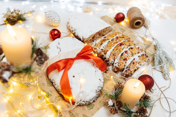 Fototapeta na wymiar Traditional German Christmas stollen made of dried fruits and nuts, sprinkled with powdered sugar on the background of a Christmas decor with candles. A festive treat.