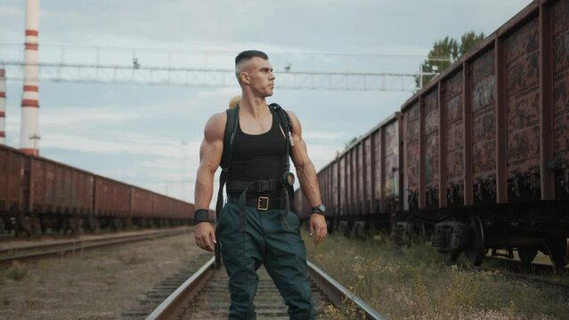 Handsome young muscular man with a balloon drager on his back stands on the rails between freight trains. Street workout