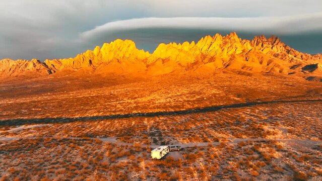 The Organ Mountains Rugged Peaks Tower Over The Chihuahuan Desert In Southern New Mexico, Camper Van Parked At Sunset - aerial pullback