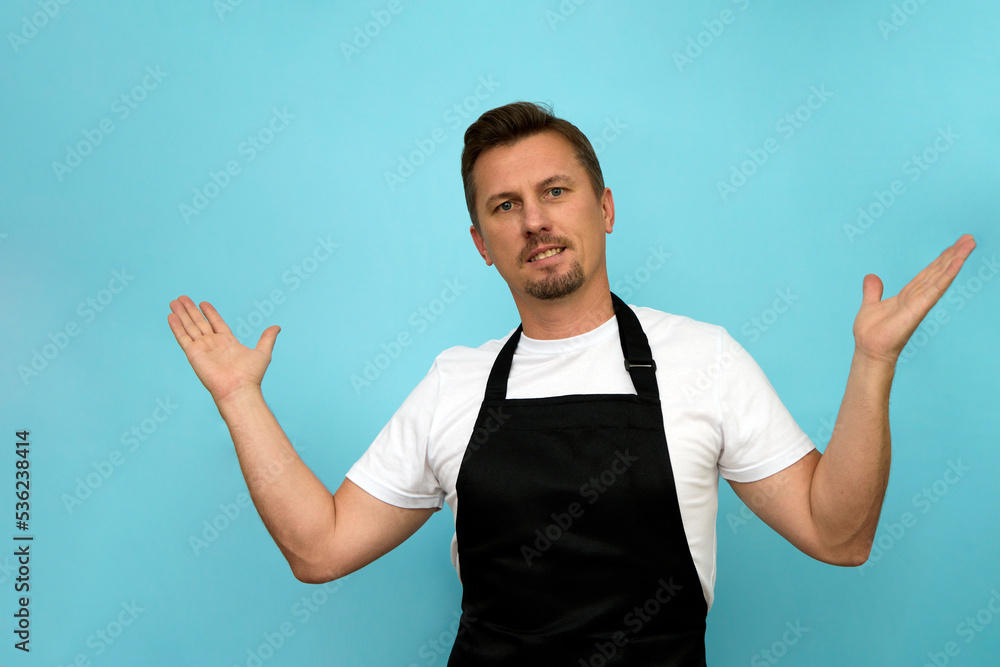 Wall mural Young barista in black apron and white t-shirt on blue background