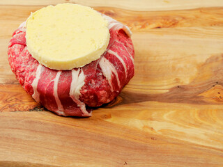 Luxury beef burger wrapped in bacon or rasher and portion of cheese on top on wooden table...