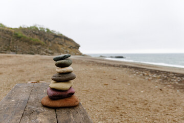 a stack of stones on a wooden bench on the beach against the background of the sea in cloudy weather