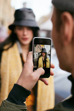 Vertical shot of unrecognizable man taking photo of stylish young woman using smartphone camera