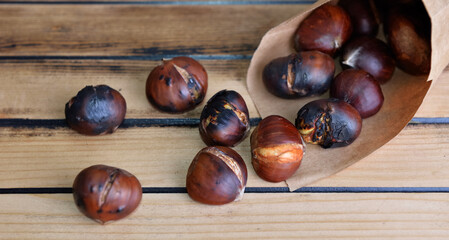 roasted chestnuts  in a papaer bag spilled on wooden table