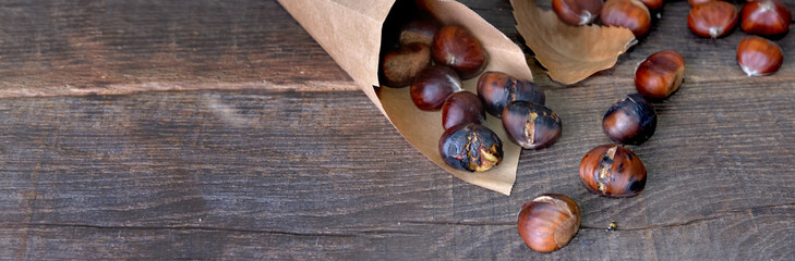 roasted chestnuts  in a papaer bag spilled on wooden table - Powered by Adobe