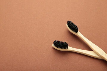 Bamboo wooden toothbrush with black brush bristles on brown background.