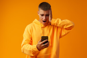 Young man expressing negativity while reading message on the mobile phone on yellow background