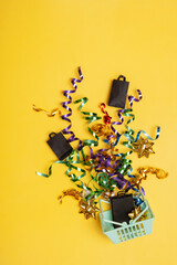 Shopping basket with spirals of tinsel and bag on top on a colored background.