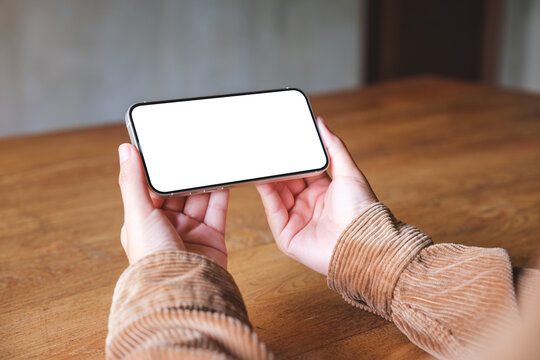 Mockup image of a woman holding mobile phone with blank desktop screen in cafe