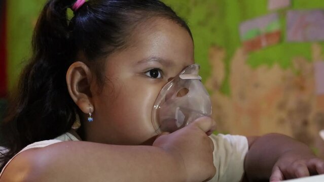 Asian Little girl making inhalation with nebulizer at home. Child asthma inhaler inhalation nebulizer steam sick cough coronavirus concept