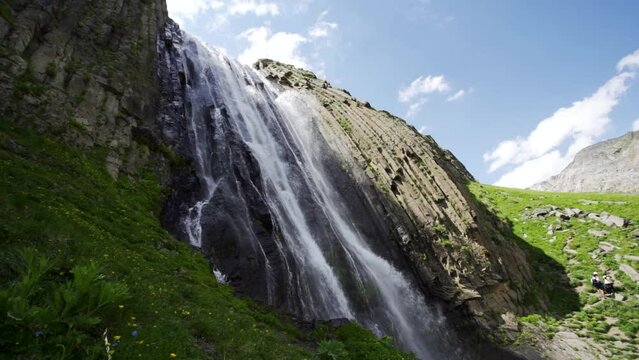 Aerial backwards beautiful waterfall cascade, alpine glacial river falls from rocks. Impressive spring nature landscape North Caucasus Kabardino-Balkaria, incredible russia scenery. Slow motion movie