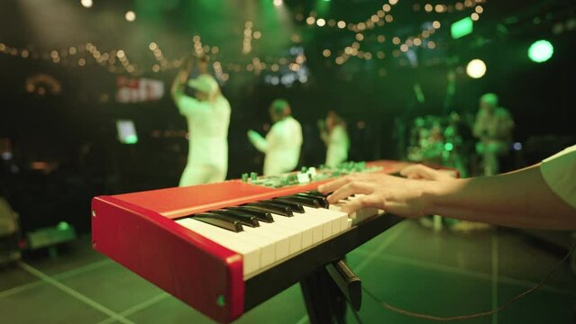 indiepop and jazz funk musical band is performing on stage of modern concert hall, closeup view of synthesizer and male hands