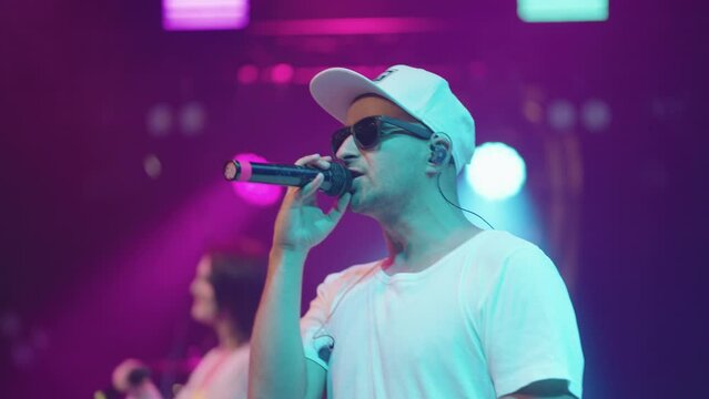 portarit of cool rapper or singer on stage during gig, man with black glasses and cap are rapping and singing