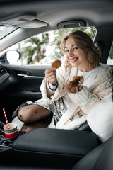 Woman passenger sitting in a car in warm woolen sweater and socks holding cookies in hands